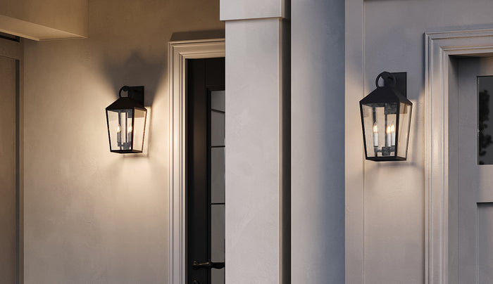 Two Cole 17" Outdoor Lantern Wall Lights with Glass Panels, finished in Matte Black, are shown glowing at dusk in a front entryway.