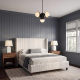 A transitional bedroom featuring the Mira 4 Globe Pendant 20", Matte Black and Satin Brass, hanging over a striped bed against gray vertical wall paneling.