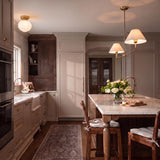 A transitional kitchen with the Holden 2 Shade Linear Pendant 57", Aged Brass featuring linen shades suspended over a white marble island with beige cabinetry - the Irving Small Flush Mount in Satin Brass is above the sink.