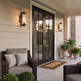 A modern farmhouse porch with two matte black Hamilton Outdoor Wall Light lanterns flanking black French doors on white siding at dusk with potted ferns.