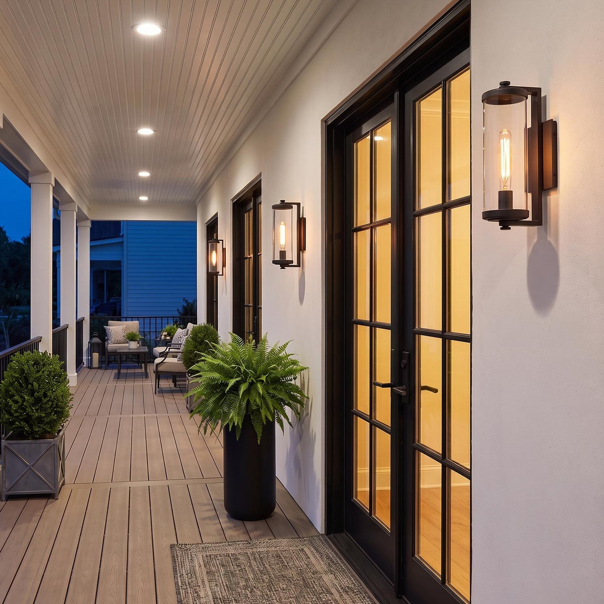 A modern farmhouse porch with the Hamilton Outdoor Wall Light, Matte Black wall lantern flanking glass doors on white stucco at twilight, featuring potted ferns.