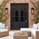 A traditional red brick patio features two matte black Colin Outdoor Wall Light Large lanterns flanking black French doors, accented by climbing jasmine and wicker furniture.