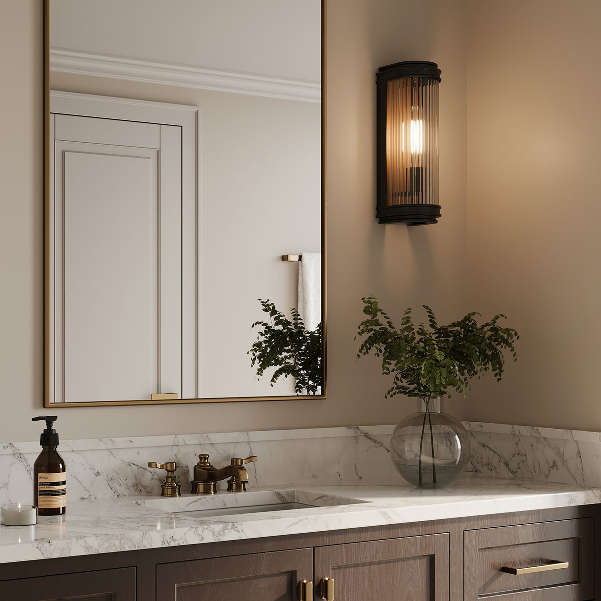 One Bristol indoor, outdoor 15" wall sconce, shown on and glowing in an upscale bathroom next to a modern brass vanity mirror