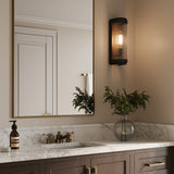 One Bristol indoor, outdoor 15" wall sconce, shown on and glowing in an upscale bathroom next to a modern brass vanity mirror