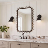 A modern farmhouse bathroom featuring two Andie Wall Sconces in matte black with frosted glass shades flanking a wavy-edged mirror over a marble vanity and beige cabinetry.