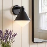 A modern farmhouse bathroom featuring an Andie Wall Sconce, Matte Black, with a frosted glass shade mounted on cream shiplap walls beside a black-framed mirror.