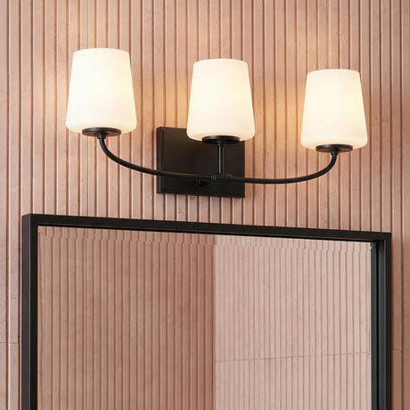 A contemporary bathroom with the Blake 3 Light Vanity, Matte Black featuring three frosted glass shades mounted above a black framed mirror against a fluted wall.