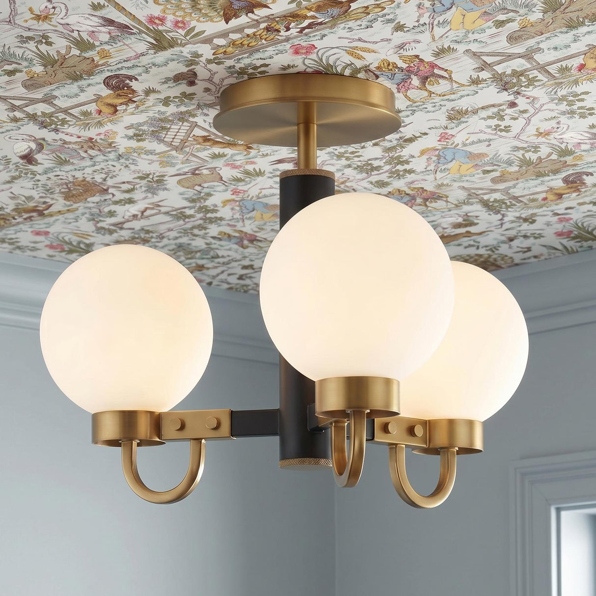 A transitional foyer with the Ryan 3 Light Semi-Flush in matte black and aged brass installed on a patterned toile wallpapered ceiling above light blue walls.