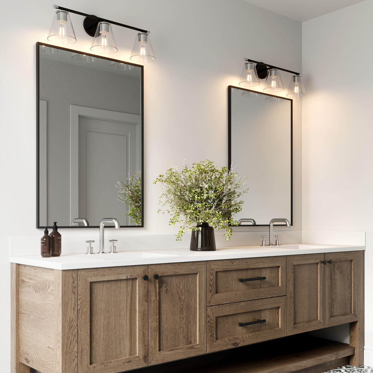 Two Carlisle 3 Light 24" Vanities, Matte Black and Chrome Finish with Clear Tapered Glass Shades, shown in a modern farmhouse style bathroom above a double vanity. 