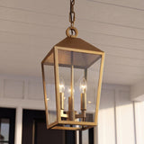 An outdoor porch with a Cole Outdoor Hanging Light, Burnished Brass with clear glass panels suspended from a white shiplap ceiling in front of a black door.