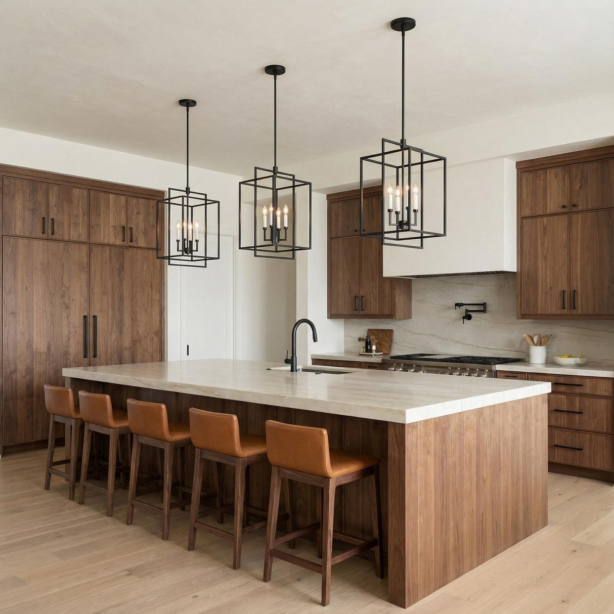 A modern kitchen features three Noa 4 Light Pendant 13", Matte Black with White lanterns over a marble island with walnut cabinets and leather stools.