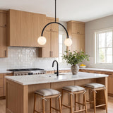 A modern farmhouse kitchen with the Risa 2 Globe Arc Pendant in matte black over a white marble island, light wood cabinets, and square tile backsplash.