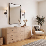 A modern bedroom featuring two Taylor Wall Sconces in matte black with white linen shades flanking a curved mirror above a light oak wood dresser on hardwood floors.