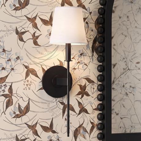 A transitional bathroom with a matte black Taylor Wall Sconce featuring a white linen shade mounted on floral wallpaper beside a black bobbin-frame mirror.