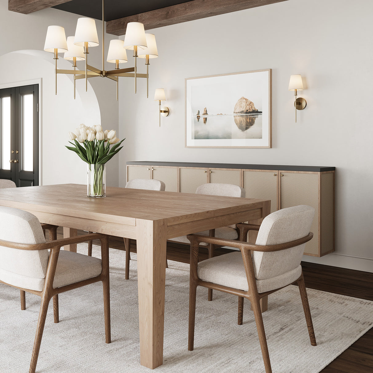 One Taylor six light Chandelier and two Taylor Wall Sconces, both in aged brass with white fabric shades, shown together in a dining room. The chandelier is hung above a light wood table and the sconces are flanking a piece of art above a console