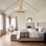 A modern farmhouse bedroom with the Taylor 6 Light Chandelier in aged brass with linen shades suspended from a vaulted beamed ceiling above a beige bed.