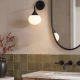 A contemporary bathroom with a matte black Talia wall sconce and frosted glass globe mounted beside an oval mirror over a white marble vanity and green square tiles.