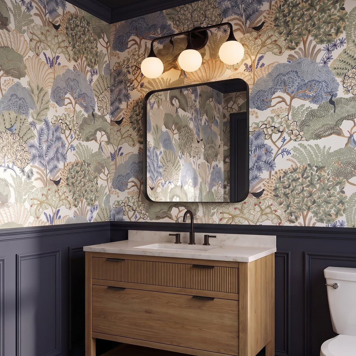 A transitional bathroom with the Talia 3 Light Vanity, Matte Black featuring white glass globes mounted above a mirror with botanical wallpaper and navy wainscoting.