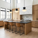 A modern kitchen with three Jayden Pendant 14", Matte Black fixtures hanging over a black stone island and natural wood cabinetry under a double-height ceiling.