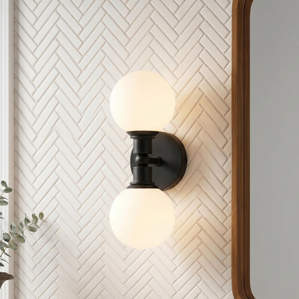A modern bathroom with a matte black Theo 2 Globe Wall Sconce featuring frosted glass globes mounted on a white herringbone tile wall beside a wood-framed mirror.