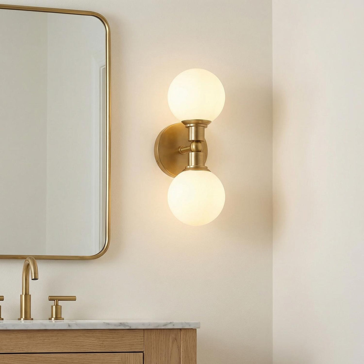 Theo 2 Globe Wall Sconce, Aged Brass globe Wall Sconce in a Modern Bathroom with a white marble vanity and oak cabinet.