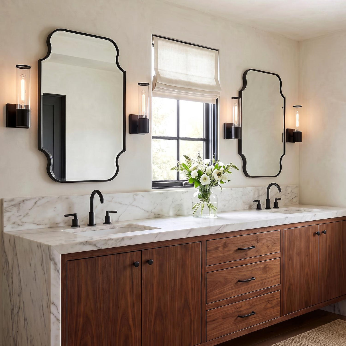 A transitional bathroom with matte black Lea Wall Sconces flanking two mirrors over a walnut vanity with a white marble waterfall countertop and matte black faucets.