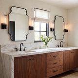 A transitional bathroom with matte black Lea Wall Sconces flanking two mirrors over a walnut vanity with a white marble waterfall countertop and matte black faucets.
