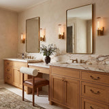 A transitional bathroom featuring four Lea Wall Sconce, Aged Brass fixtures flanking gold-framed mirrors over a marble double vanity and light oak wood cabinetry.