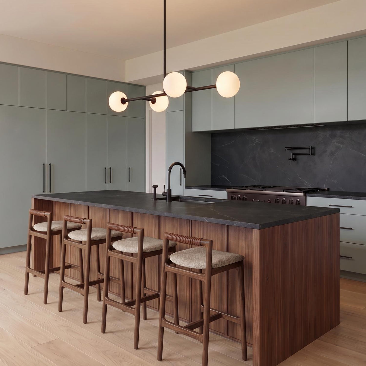 A modern kitchen with a matte black linear pendant featuring frosted glass globes over a wood island with black stone counters and sage green cabinetry.