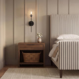 A transitional bedroom with a matte black Mason 1 Light Wall Sconce mounted on beige paneling above a walnut nightstand and striped bed.