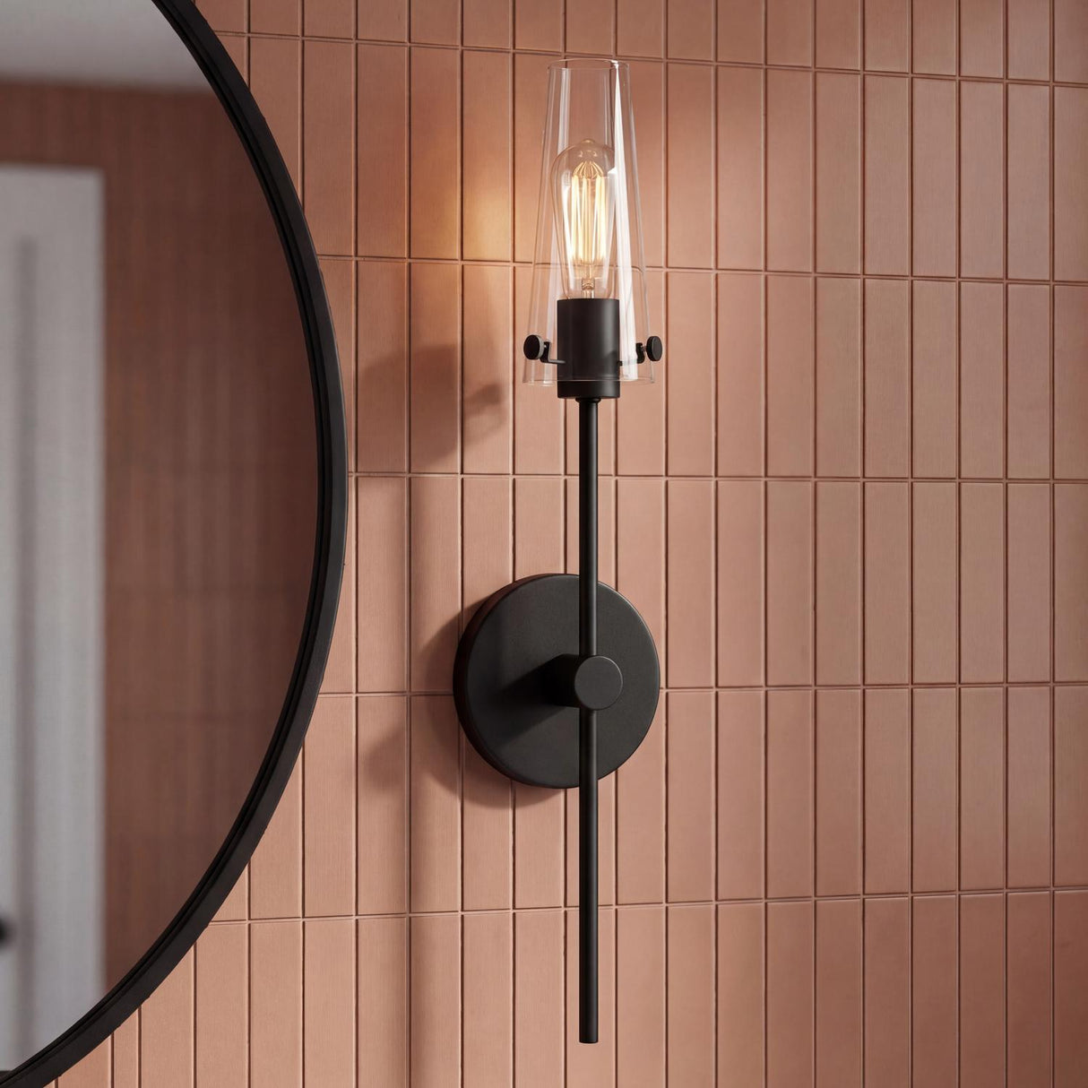 Mason 1 Light Wall Sconce Matte Black linear Wall Sconce in a Modern Bathroom with terracotta tile and a round mirror.