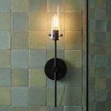 A modern bathroom with a matte black Mason 1 Light Wall Sconce featuring a tapered clear glass shade mounted on a green zellige square tile wall.