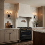 A transitional kitchen with two matte black Mason 2 Light Wall Sconces flanking a plaster range hood above a black stove and white tile backsplash.