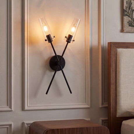 A transitional bedroom featuring a matte black Mason 2 Light Wall Sconce with clear glass cylinders mounted inside wall molding beside a walnut wood headboard.