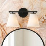 A contemporary bathroom with a matte black vanity wall light featuring tapered opal glass shades mounted above a round black-framed mirror on a veined marble tile wall.