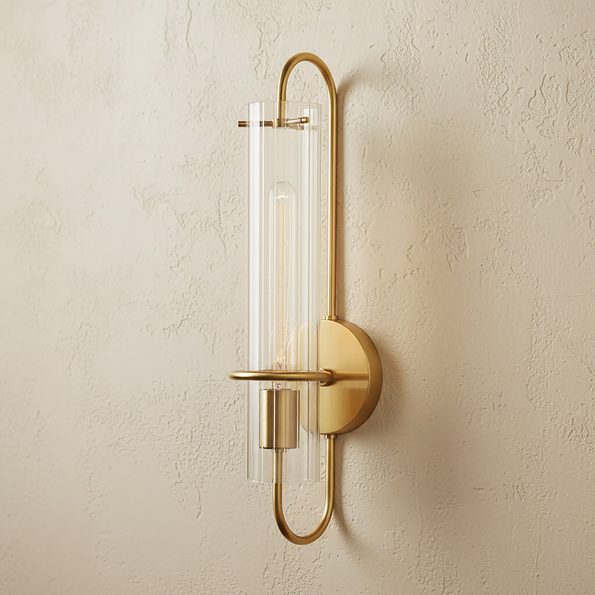 Camie Wall Sconce 20", Aged Brass with clear ribbed glass shade shown on a biege textured wall.