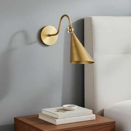Faye Adjustable Metal Wall Sconce, Aged Brass - Brass sconce beside bedside table and upholstered headboard