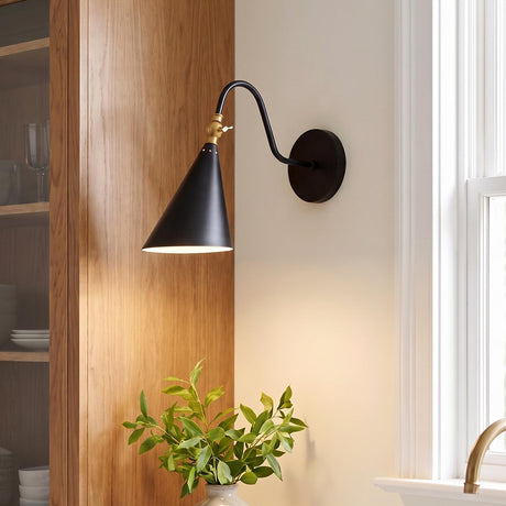 A modern kitchen featuring the Faye Adjustable Metal Wall Sconce, Black with Aged Brass mounted on a wall beside a natural wood cabinet and window.