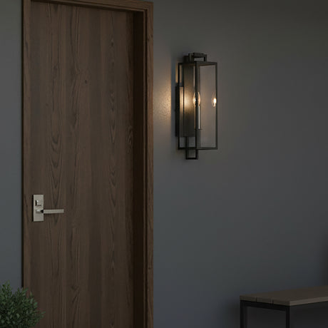 Everett Outdoor Wall Light, Small, Forged Iron Black - A modern outdoor wall light with a black metal frame and clear glass panels is mounted on a gray wall next to a wooden door.