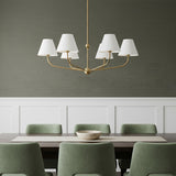 Banks 6 Light Chandelier 40, White and Brass - A brass chandelier with white shades hangs over a dark wood dining table with green chairs.