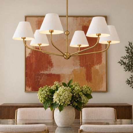 A transitional dining room features a brushed brass chandelier with white fabric shades suspended above a glass dining table with a green hydrangea centerpiece.