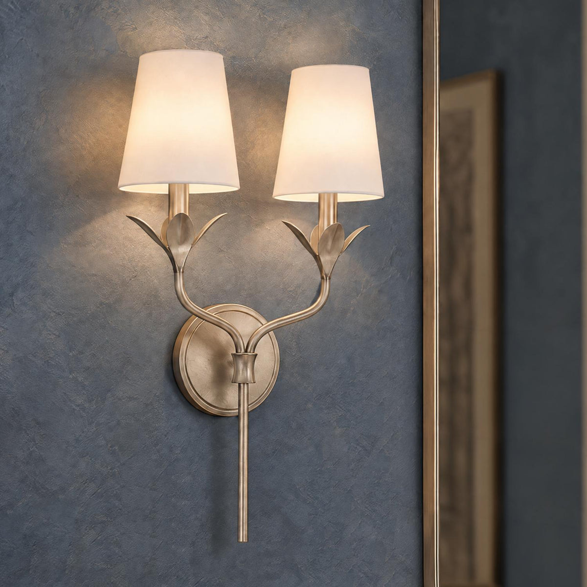 A transitional living room featuring an Alice Double Wall Sconce in antique silver with tapered white fabric shades mounted on a textured slate wall.