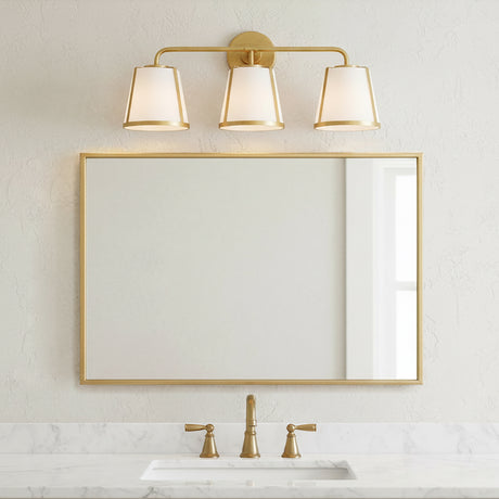 Hoyt 3 Light Vanity Light, Antique Gold with Opal Glass, shown above a single sink and mirror in a neutral decorated bathroom.