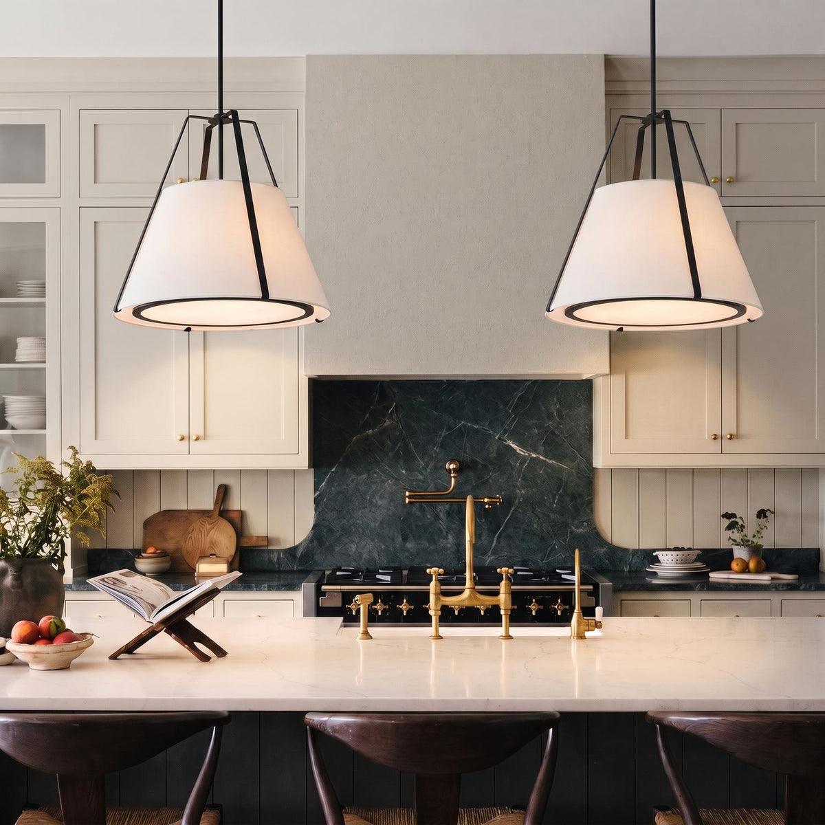 A modern farmhouse kitchen with two matte black cage pendants featuring white linen shades suspended over a white marble island with a dark green marble backsplash.