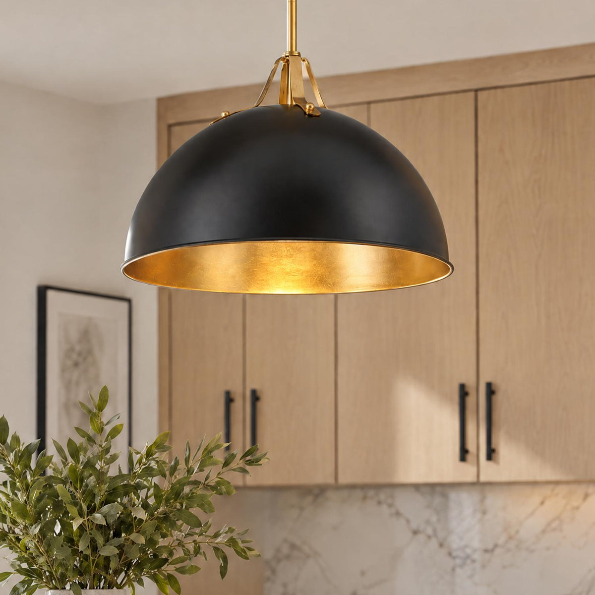 A modern kitchen featuring a matte black dome pendant with an antique gold interior suspended over an island before light wood cabinets.