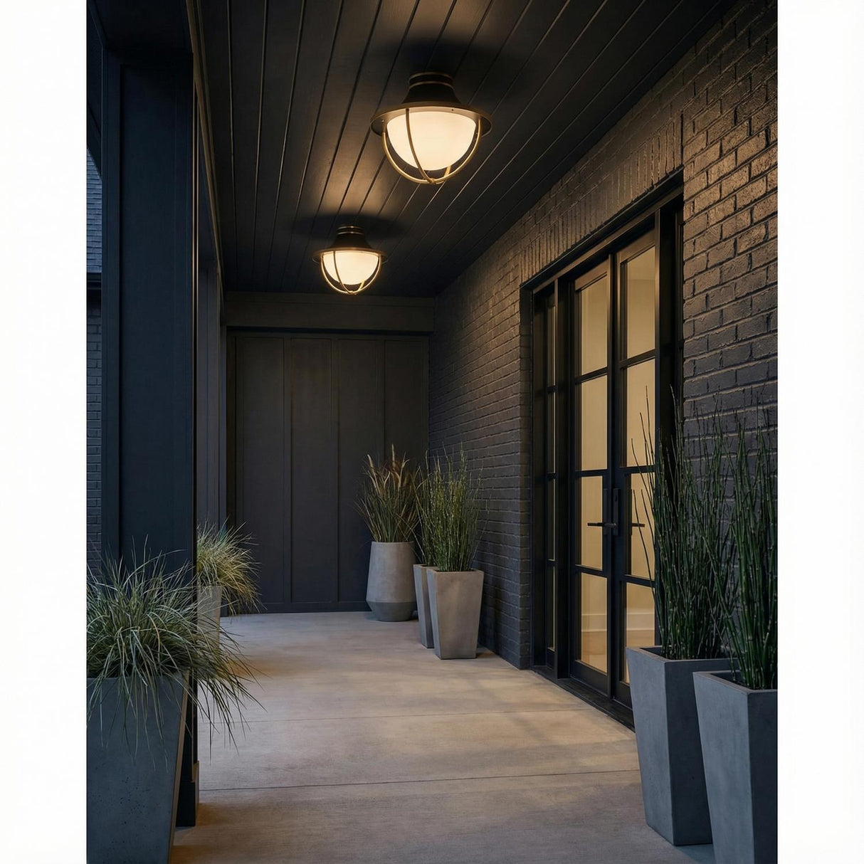 Tobin Outdoor Flush Mount, Black and Brass geometric globe flush mount in a Modern Outdoor with a dark brick wall and concrete planters.