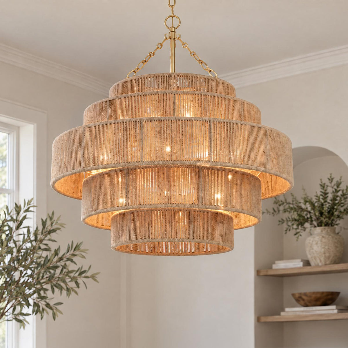 A coastal living room features the Sorelle 20 Light Chandelier in jute and soft brass hanging near an arched wall niche with floating wood shelves.