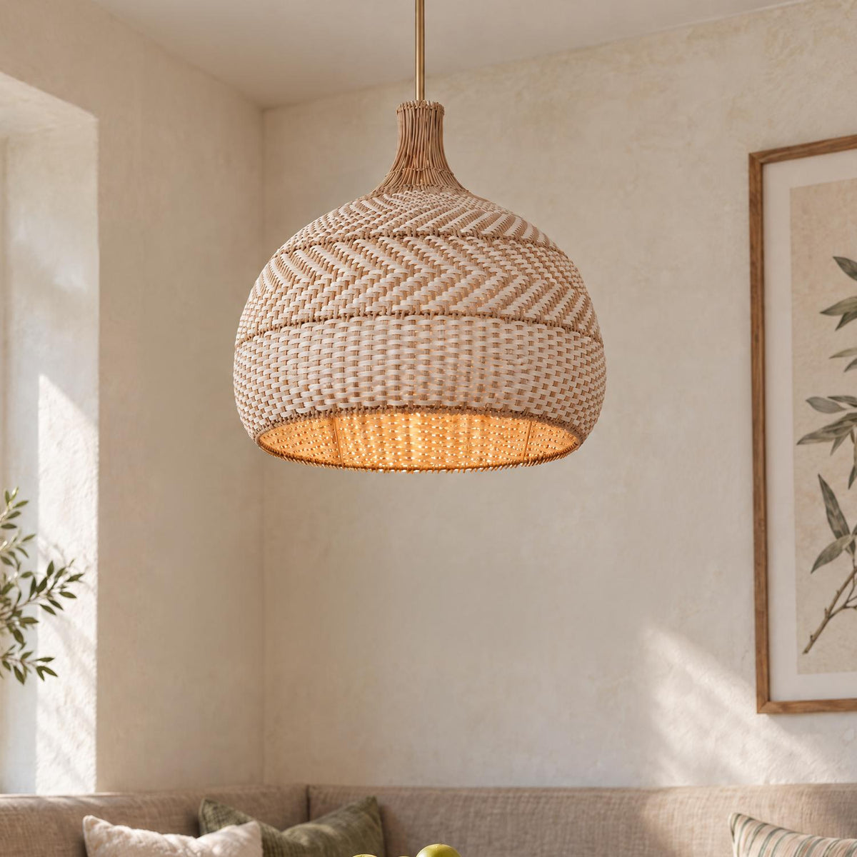 A coastal dining nook features the Sienna Large Pendant in woven rattan and soft brass hanging above a neutral cushioned banquette framed by botanical wall art.