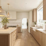 A coastal kitchen with two Sienna Extra Large Pendants in rattan and soft brass over a marble island featuring light wood fluted cabinets and gold hardware.
