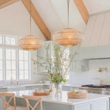 A coastal kitchen with two rattan and soft brass saucer pendants over a white island featuring light blue cabinets and wood beams on a vaulted ceiling.